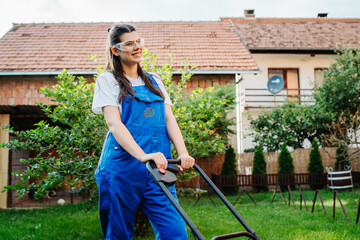 One young caucasian woman is using lawn mower to mow grass in her backyard