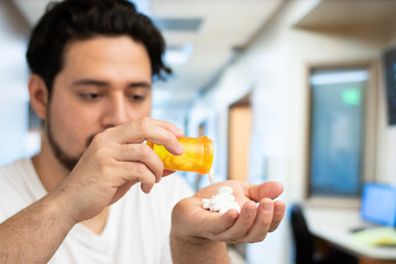 Fototapeta premium Close up of man putting many pills in his hand in a hospital room with copy space