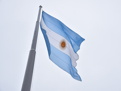 Close-up of a flag of argentina flying with the wind on the top of a flagpole with the sky as background.