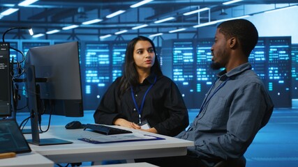 Multiracial team of IT engineers in server room brainstorming ways to fix equipment storing...