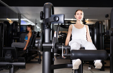 Sportive young woman doing exercises on leg extension device in well-equipped gym
