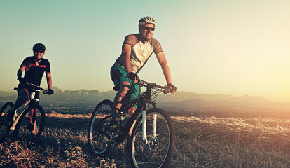 Fototapeta premium Sunset, men and friends in bicycle race with helmet, exercise and adventure trail in nature together. Cycling, fitness and people with mountain bike in evening for outdoor workout, energy and smile