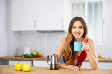Portrait of smiling young woman drinking morning coffee at home kitchen
