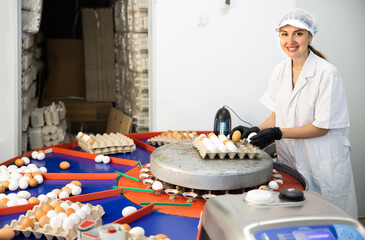 Focused young woman farmer worker in white coat sorting and labeling chicken eggs, putting eggs to...