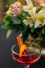 whiskey cocktail with cinnamon and orange in front of bouquet of flowers during daytime party