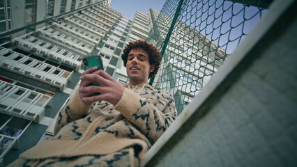 Smiling man texting cellphone at urban buildings backdrop closeup bottom view.