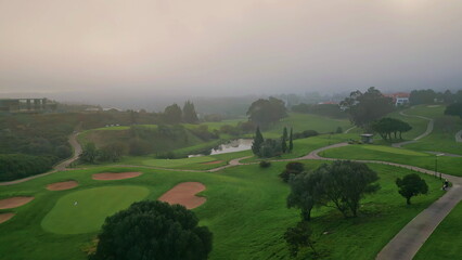Drone misty morning descending on golf course. Fog covering field greenery 