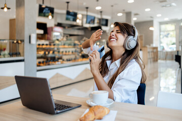 Beautiful and happy young woman sitting and eating delicious rolls in bakery or fast food. She also...