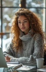 young woman writing in a notebook at a glass table with a laptop beside her