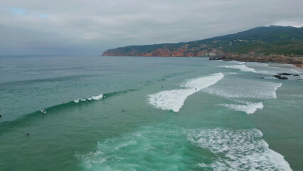 Surfers catching ocean waves at scenic coastline aerial view. Rugged cliffs