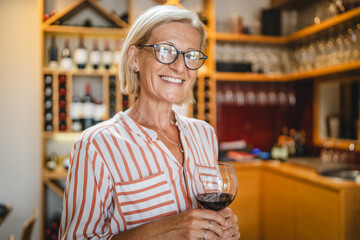 Portrait of senior woman stand and hold glass of wine in the winery