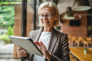 Portrait of senior woman winemaker stand and use tablet in the winery