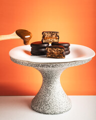 alfajores de dulce de leche bañados en chocolate negro apilados sobre base y plato con ondas...