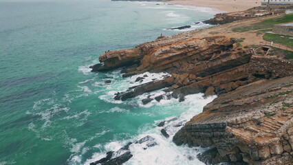 Waves colliding rocky cliffs at pristine coastline drone view. Turquoise ocean 