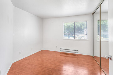 A vacant room with hardwood floors and white walls with a large mirror. Great for virtual staging images