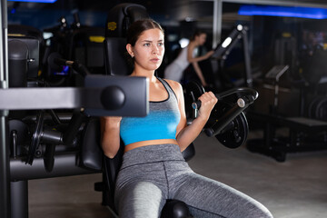 Fototapeta premium Girl does exercises to strengthen muscles of arms and shoulders, increase muscle volume and contouring. Athletics, self-study in fitness center