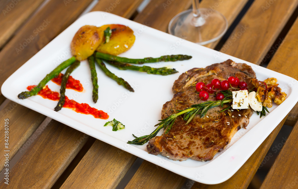 Wall mural Fried beef loin decorated with red currant, walnut and rosemary with grilled vegetables on plate on wooden background..