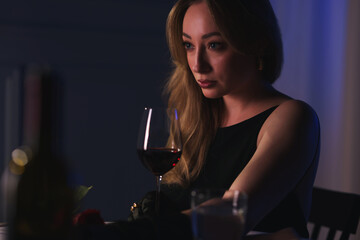 Elegant young woman with glass of wine at table indoors in evening