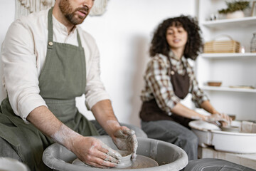 Man and woman potters using pottery wheels to craft clay vases in studio setting, focused on creativity and craftsmanship.