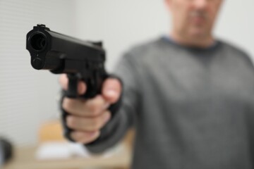 Dangerous criminal with gun indoors, selective focus. Armed robbery