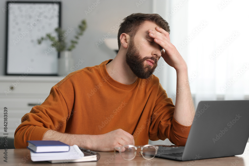 Wall mural Overwhelmed man sitting with laptop at table indoors