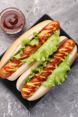 Tasty hot dogs with lettuce, ketchup and mustard on grey textured table, flat lay