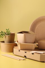 Eco friendly food packaging. Paper containers, tableware and green twigs on pale yellow background
