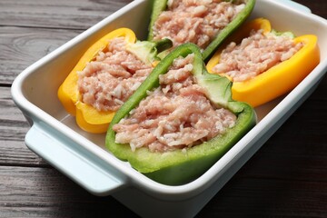 Raw stuffed peppers in dish on wooden table, closeup