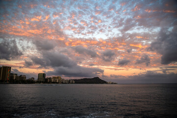 Fototapeta premium A stunning sunset over Waikiki Beach, Hawaii, with vibrant clouds and the iconic Diamond Head in the background.