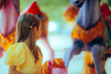 Little Girl in a Fun Carousel at an Amusement Park. Happy child being entertained in a funfair...