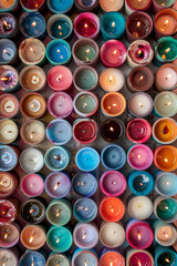 An abundant collection of small candles in various colors and shapes, tightly arranged to fill the entire frame. The candles display a range of hues from pastel to bright.