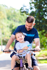 Obraz premium A Brazilian father carries his young son on the bicycle. They are having fun and enjoying the moment together. Father's Day.