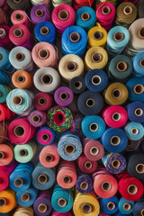 A tightly packed collection of spools of thread in various colors, filling the entire frame. The threads come in shades of red, blue, green, yellow, and pink, creating a vibrant and crafty background.