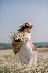 Happy woman in a field of daisies with a wreath of wildflowers on her head. woman in a white dress...