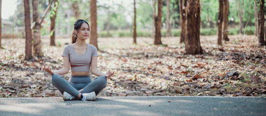 A woman is sitting on the ground in a park, practicing yoga. The scene is peaceful and serene, with...