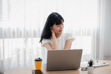 Young woman working on a laptop at a home office desk with coffee and plant, bright natural light...