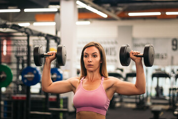 woman athlete training with dumbbells in front of the mirror in a gym