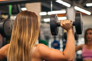 back view of a blonde woman athlete training with dumbbells
