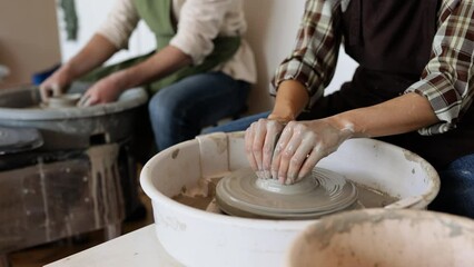 Man and woman working together on potters wheel creating clay pottery. Hands shaping clay vase in artistic studio. Creativity, craftsmanship, and teamwork.