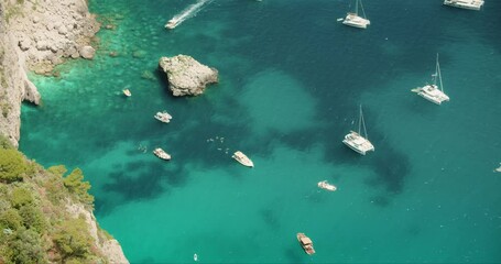 Boats floating on turquoise water near rocky coastline at Capri Italy. Top down view of sea with pleasure yachts in summer sunny day.