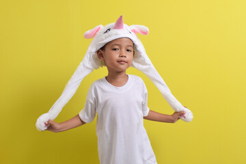 Asian little boy posing wearing cute character hat on yellow background. Portrait of a cute Asian boy