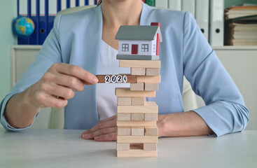 Woman Playing Jenga With House Model and 2024 Block