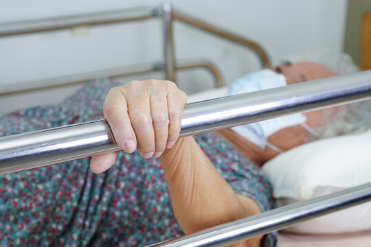 Asian elder senior woman patient holding bed rail while lie down with hope waiting her family in hospital.