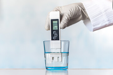 Water quality meter tester submerged in drinking glass, on blue background. Measuring harmful...