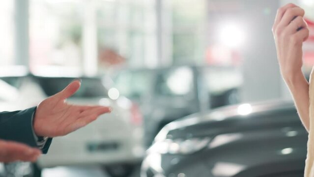 Hands, key and car dealership with salesman and customer in showroom for purchase discussion. Transport, buying or deal with automobile dealer handing keys to buyer after sale pitch for auto vehicle