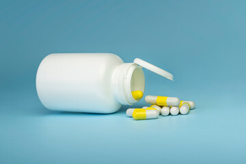 opened white plastic bottle and yellow vitamins pills on the blue background