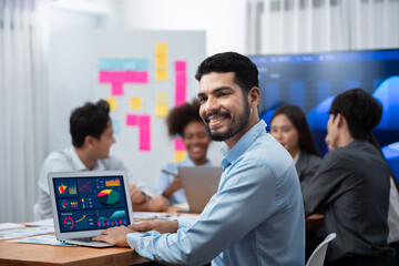 Portrait of happy and smiling businessman with group of coworkers on meeting with screen display...