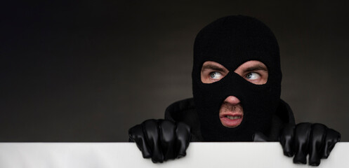 An evil thief in mask looks out from behind a white board. Space for text and design. copy space....