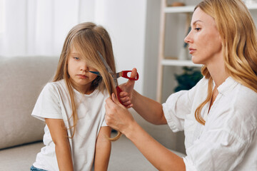 Woman carefully trimming young girl's hair with scissors while gently combing through strands in...