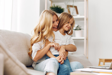 Loving mother and daughter share a warm embrace on a cozy couch in a sunlit living room